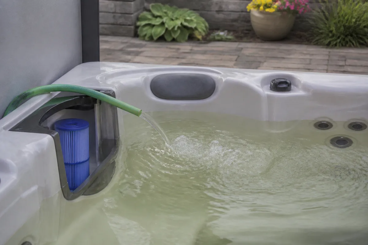 Garden hose filling a residential hot tub with tinted source water