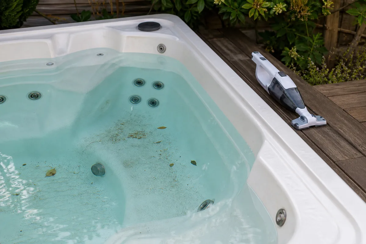 Handheld hot tub vacuum beside a spa with debris on the floor